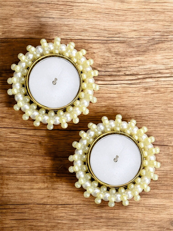 Two pearl-framed candles on a wooden surface