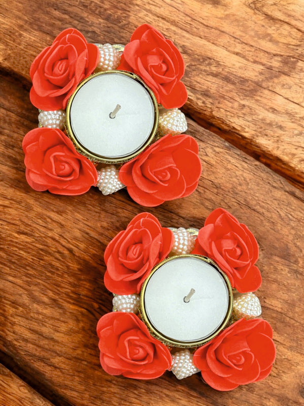 Decorative candle holders with red flowers and pearls on a wooden surface
