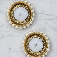 Two round candle holders with gold rims and pearl-like beads on a marble surface.