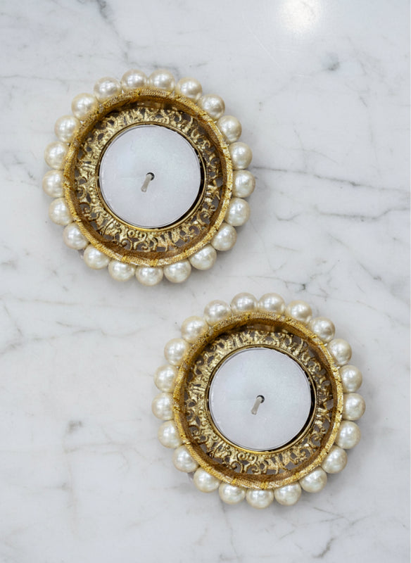 Two round candle holders with gold rims and pearl-like beads on a marble surface.