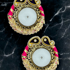 Pair of ornate earrings with gold, pink, and black design on a dark marble background