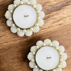 Two pearl-framed candles on a wooden surface