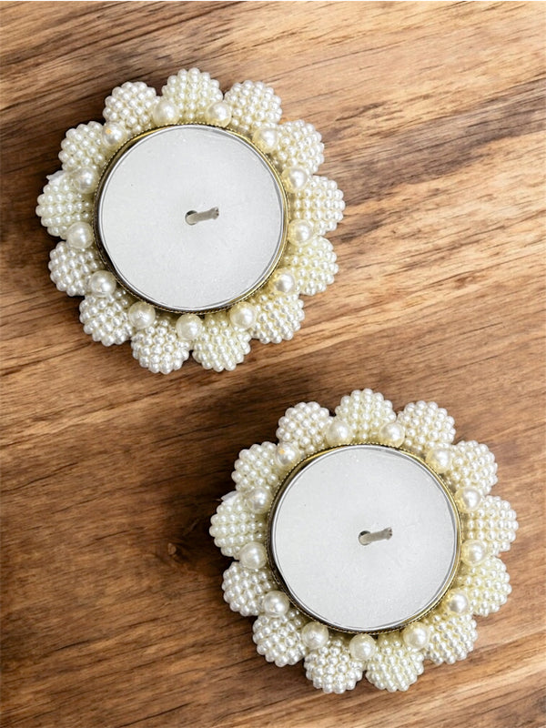 Two pearl-framed candles on a wooden surface