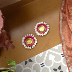 Decorative earrings with pink and gold design on a brown surface.