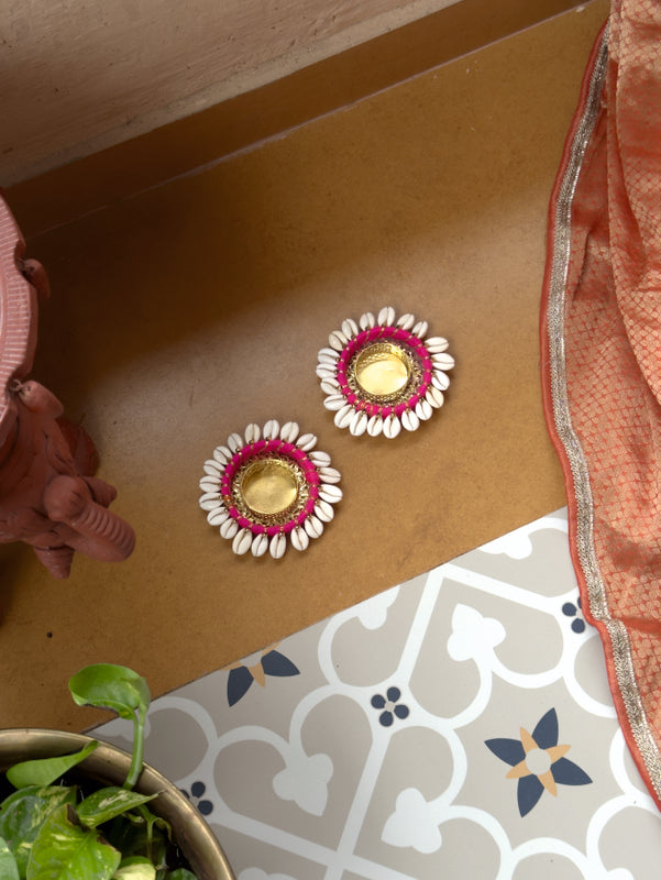 Decorative earrings with pink and gold design on a brown surface.