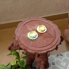 Decorative red stool with gold and green circular designs on a patterned surface.
