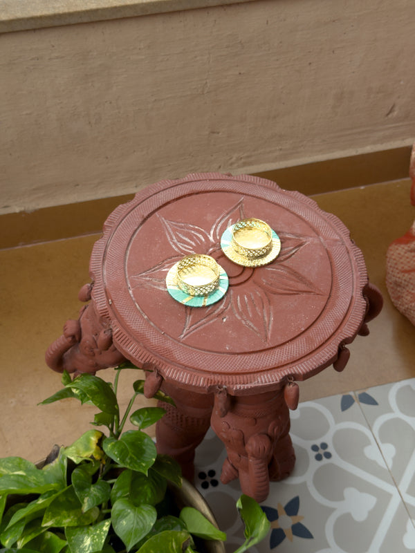 Decorative red stool with gold and green circular designs on a patterned surface.