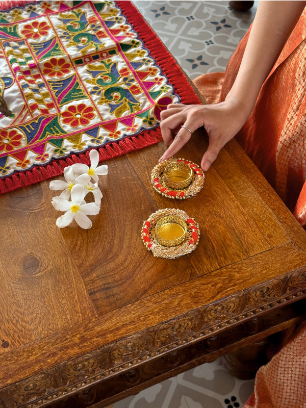 Decorative setting with colorful fabric, flowers, and traditional items on a wooden table.