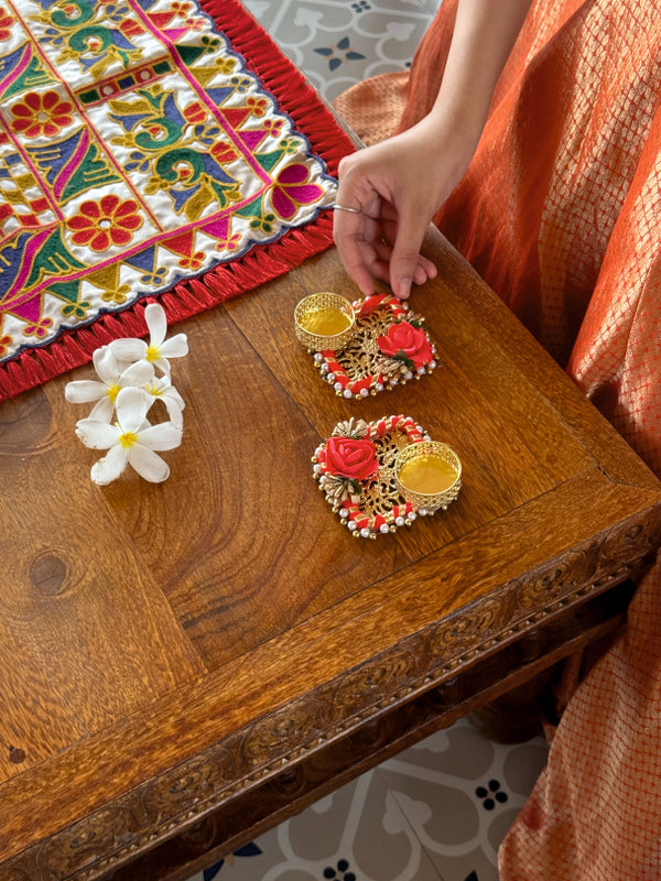 Decorative earrings on a wooden table with a colorful embroidered cloth in the background