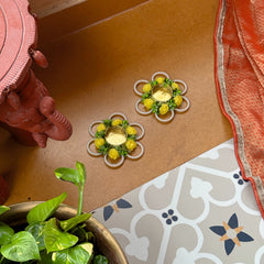 Decorative flower-shaped candles on a brown surface with a plant and patterned fabric in the foreground.