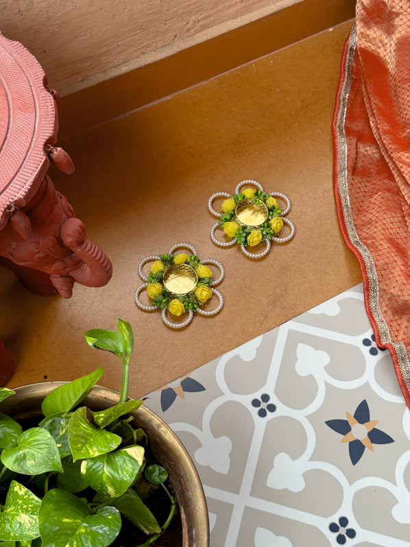 Decorative flower-shaped candles on a brown surface with a plant and patterned fabric in the foreground.