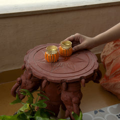 Person holding two small decorative items on a pink stand with a plant in the foreground.