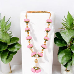 Pink floral earrings on a white stand with green plants on either side.