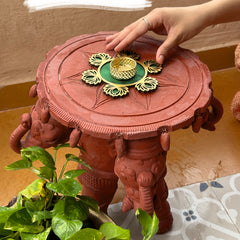 Decorative pink table with gold decorations, hand reaching towards it, green leaves in foreground
