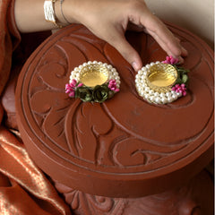 Decorative earrings with pearls and pink flowers on a brown round object.