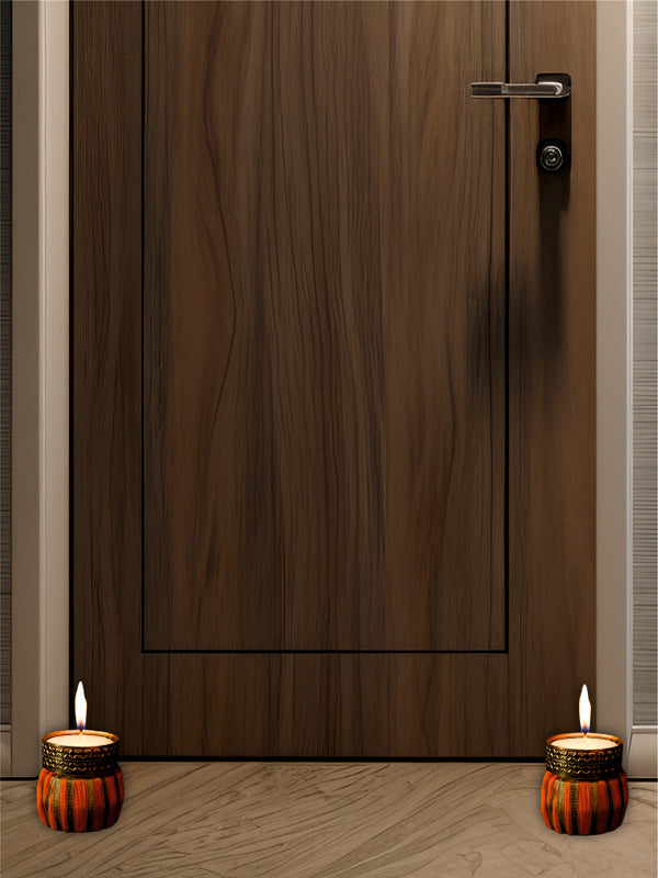 Wooden door with two lit candles on either side on a wooden floor.