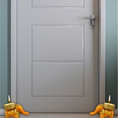 Gray door with two small orange candle holders shaped like elephants on a light gray floor.