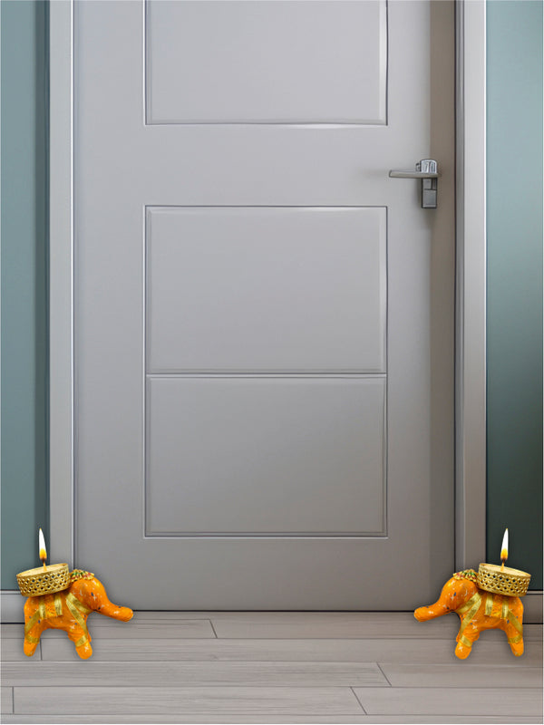 Gray door with two small orange candle holders shaped like elephants on a light gray floor.