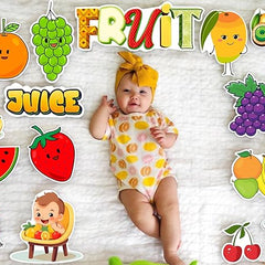 Baby in a onesie surrounded by colorful fruit-themed stickers on a textured background