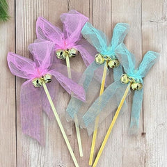 Decorative sticks with pink and blue ribbons and gold bells on a wooden surface
