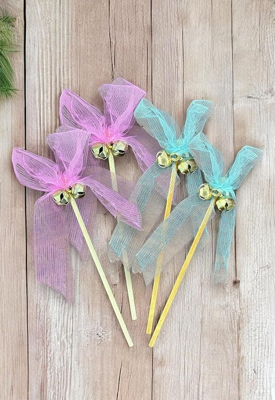 Decorative sticks with pink and blue ribbons and gold bells on a wooden surface