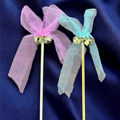 Two decorative hair sticks with pink and blue ribbons on a dark blue fabric background