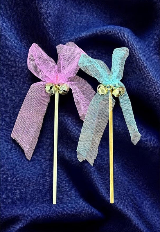 Two decorative hair sticks with pink and blue ribbons on a dark blue fabric background