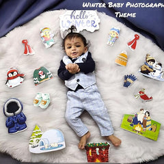 Baby in a winter-themed outfit surrounded by winter-themed props on a fluffy white surface.