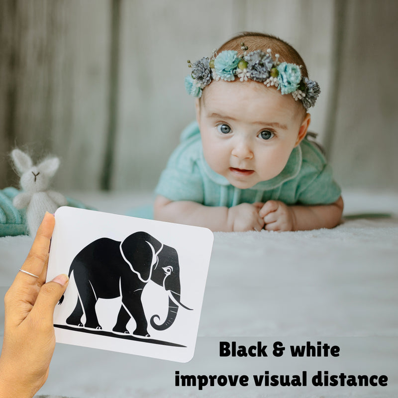 Baby lying on a bed with a person holding a card with an elephant illustration.