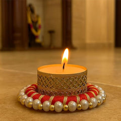 Decorative candle with a gold holder and red and gold base on a wooden surface.