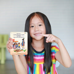 Young girl pointing to a colorful educational card held in her hand.