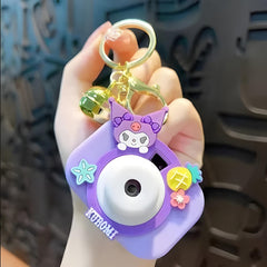 Purple camera-shaped keychain with a character design held by a hand against a blurred background