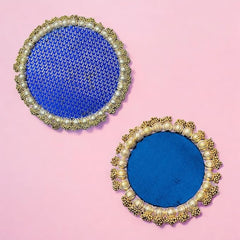 Pair of round blue coasters with gold and pearl embellishments on a pink background