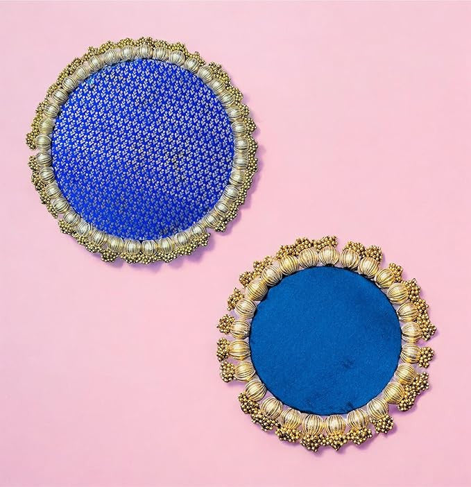Pair of round blue coasters with gold and pearl embellishments on a pink background