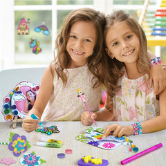Two young girls sitting at a table with art supplies, smiling at the camera.