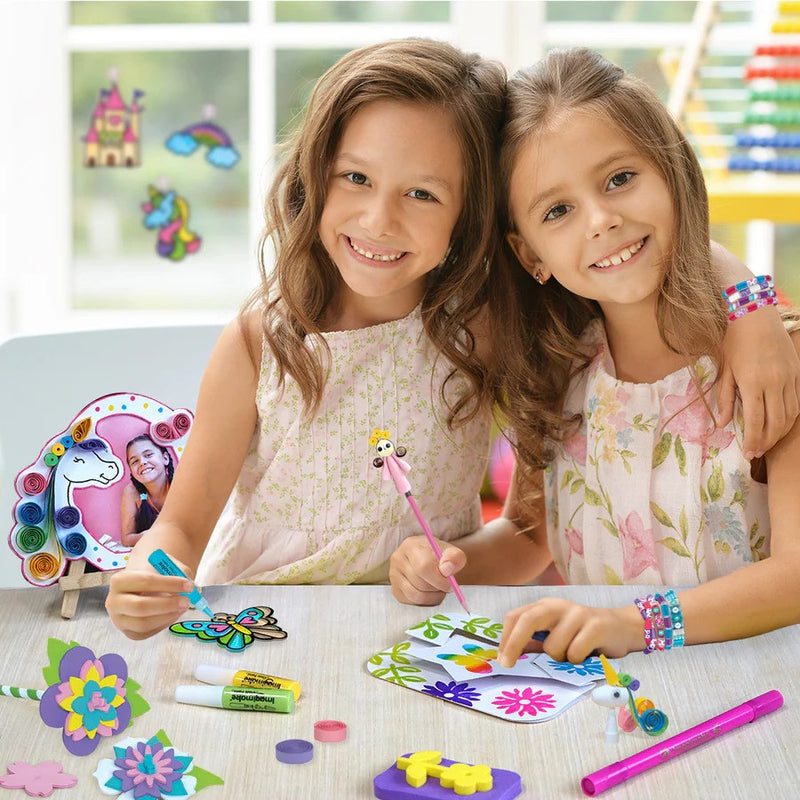 Two young girls sitting at a table with art supplies, smiling at the camera.