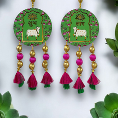 Pair of earrings with green circular designs featuring cows, gold and pink beads, and tassels on a white background.