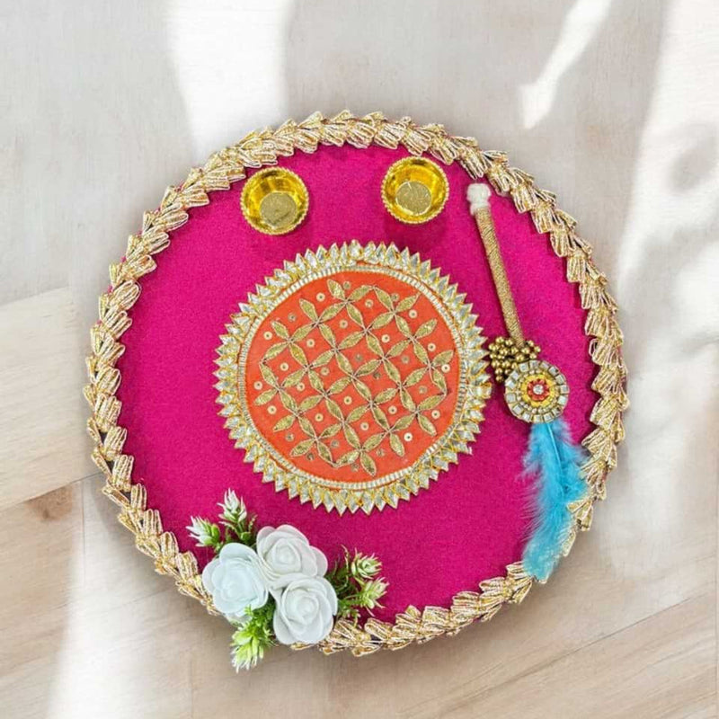 Decorative pink round tray with gold embroidery, flowers, and decorative items on a light background